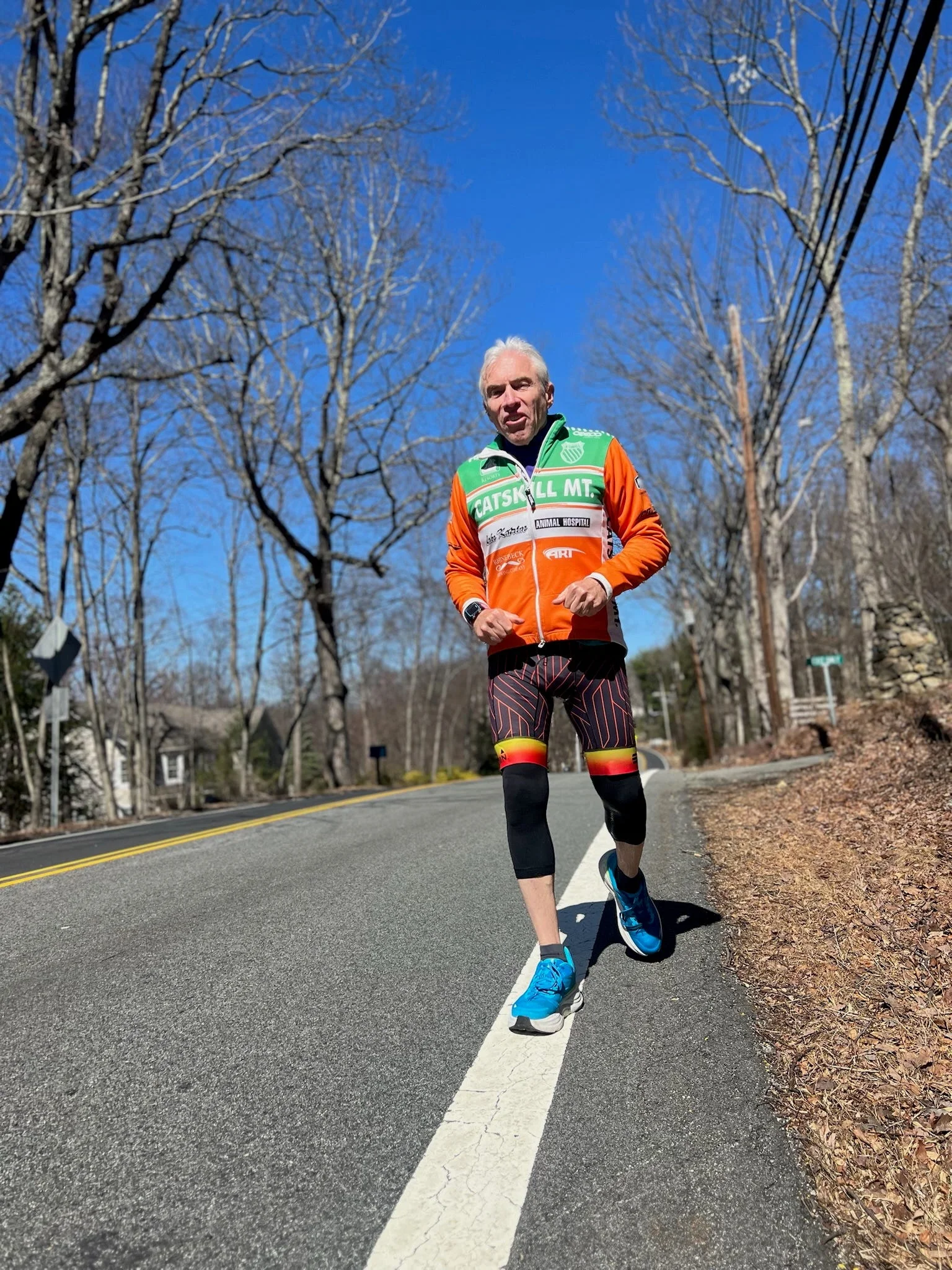 Man running on a sunny road wearing an orange and green jacket, colorful shorts, and bright blue shoes. Man running on a sunny road wearing an orange and green jacket, colorful shorts, and bright blue shoes.