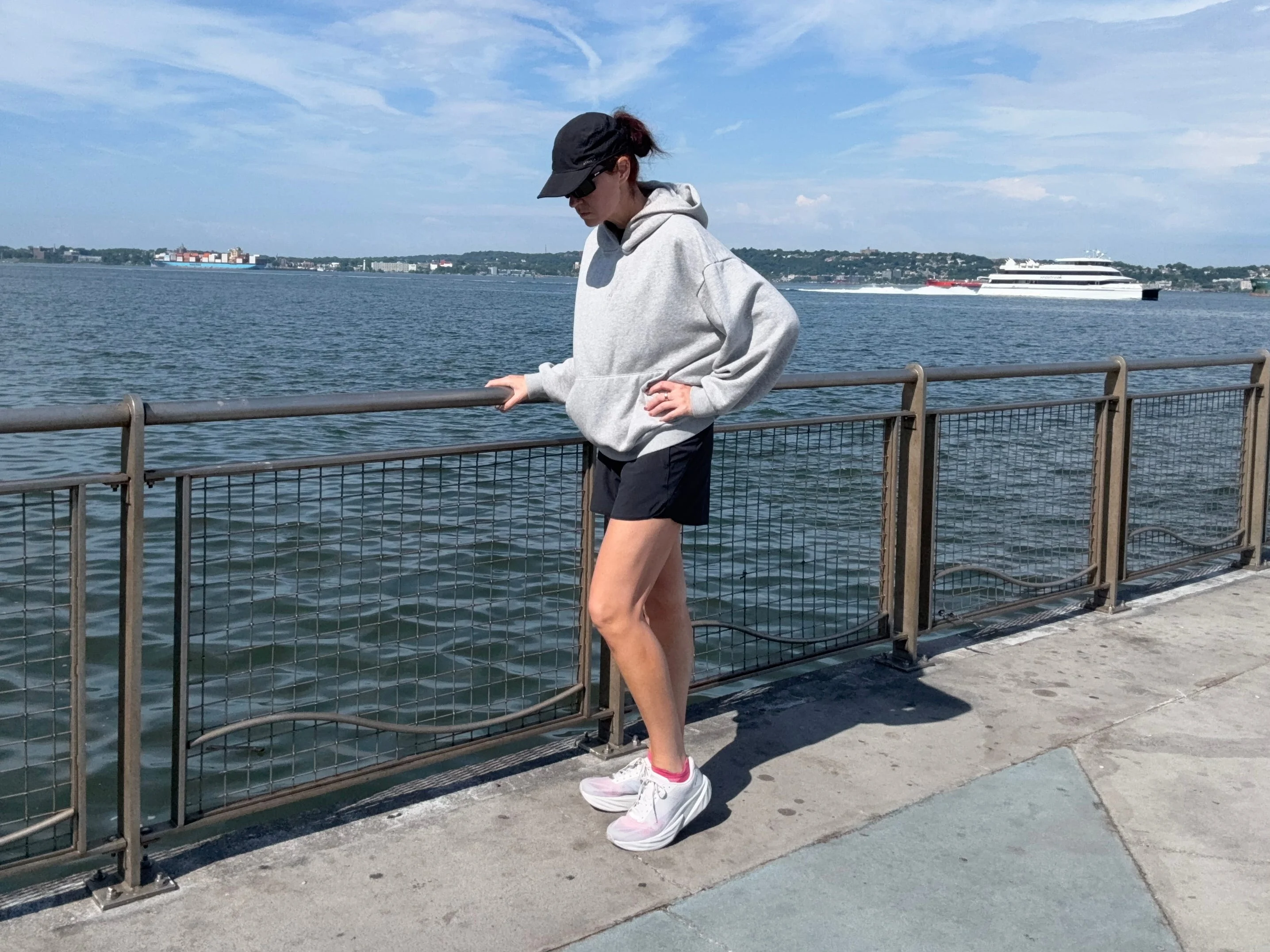 Person in activewear standing by a waterfront railing on a sunny day, sporting New Balance FuelCell Rebel V5 Person in activewear standing by a waterfront railing on a sunny day, sporting New Balance FuelCell Rebel V5