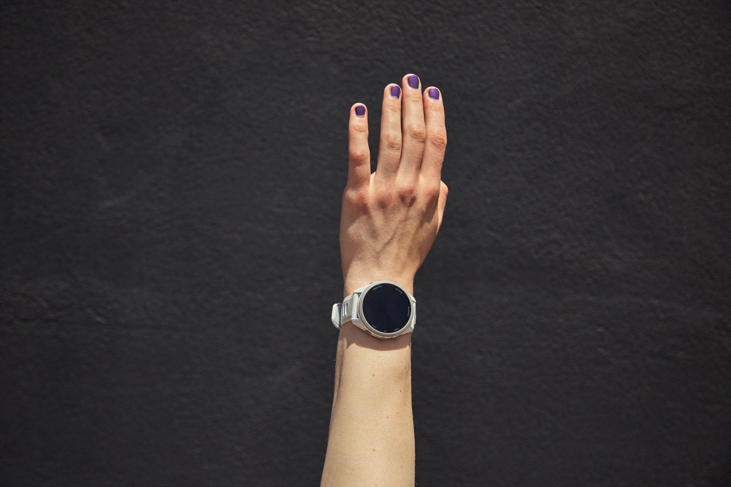 Hand with purple nails wearing a smartwatch against a dark background. Hand with purple nails wearing a smartwatch against a dark background.