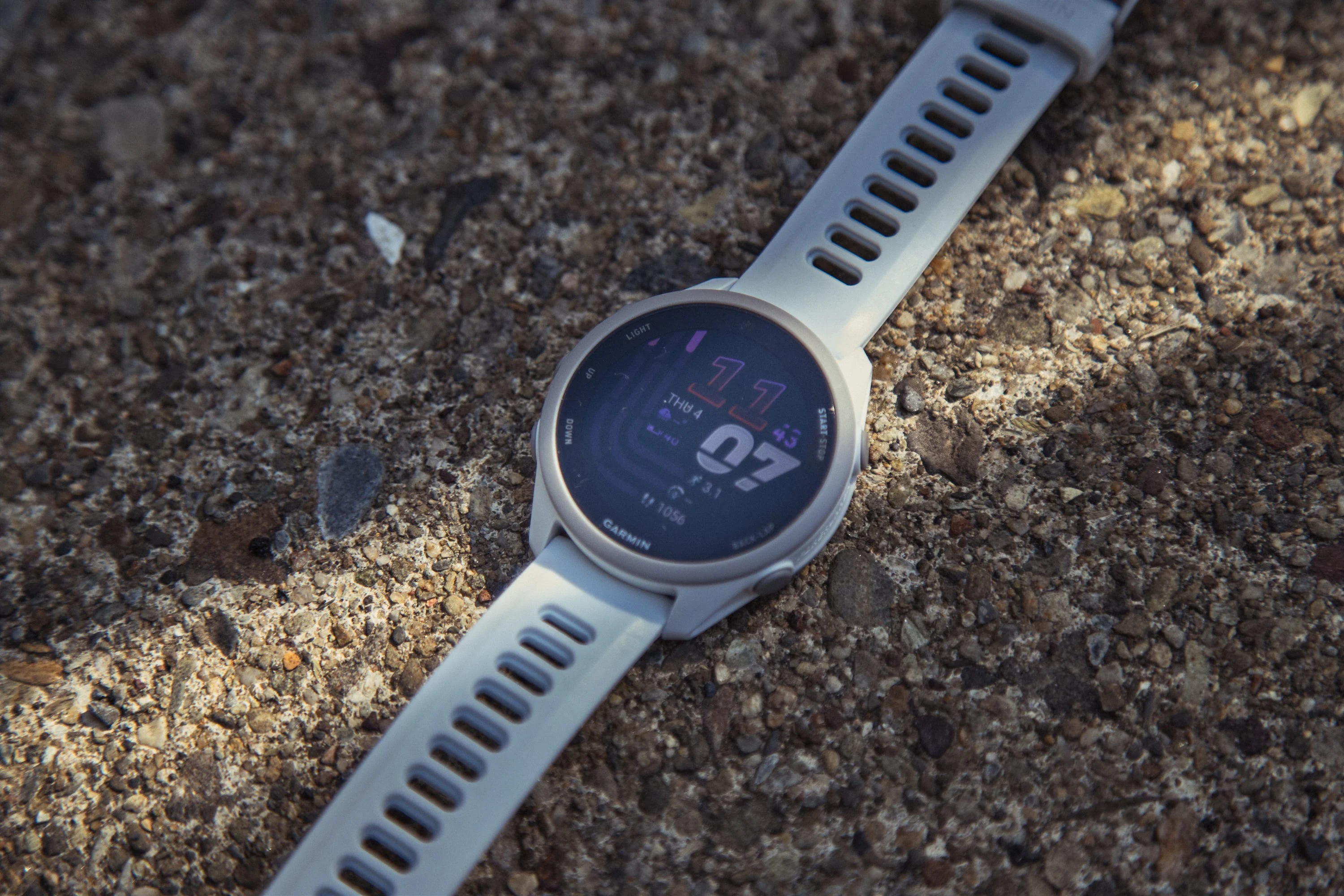 Smartwatch with white strap on textured surface displaying time and date. Smartwatch with white strap on textured surface displaying time and date.