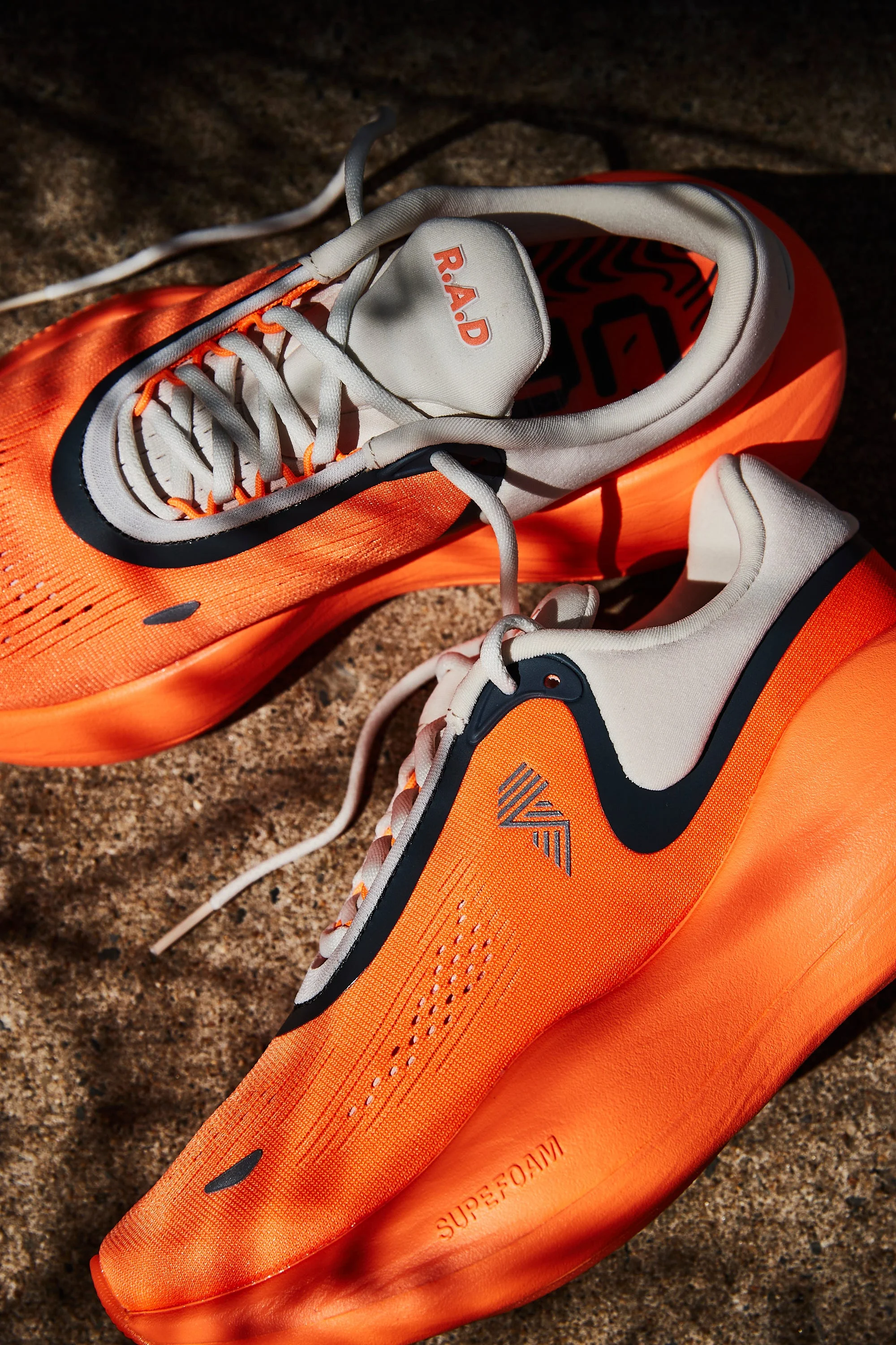 RWD Bright orange running shoes with white and black accents on a stone surface.