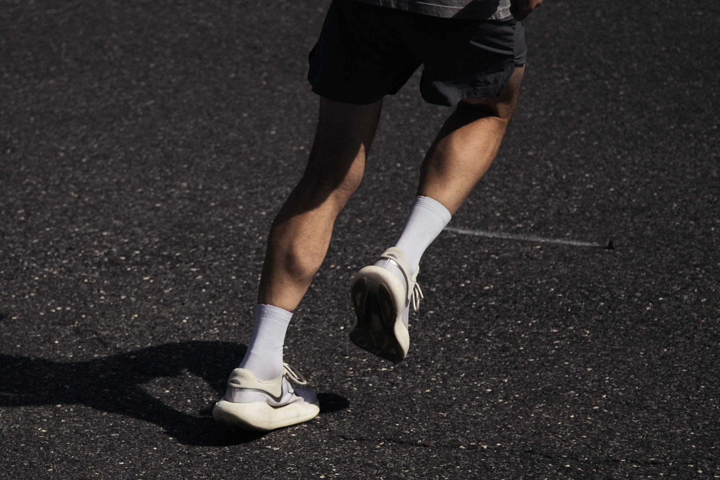 Person running on asphalt in shorts and white sneakers. Person running on asphalt in shorts and white sneakers.
