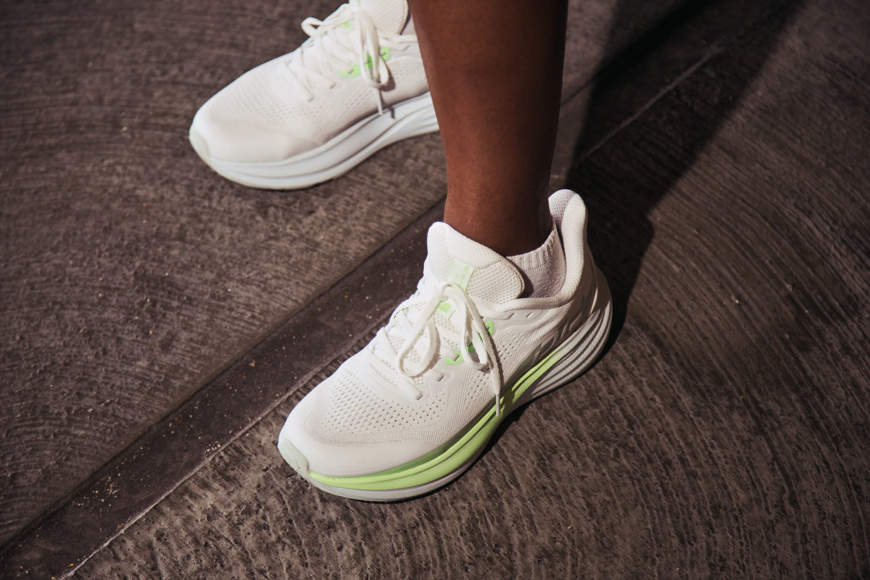 Person wearing white running shoes with green accents on concrete. Person wearing white running shoes with green accents on concrete.