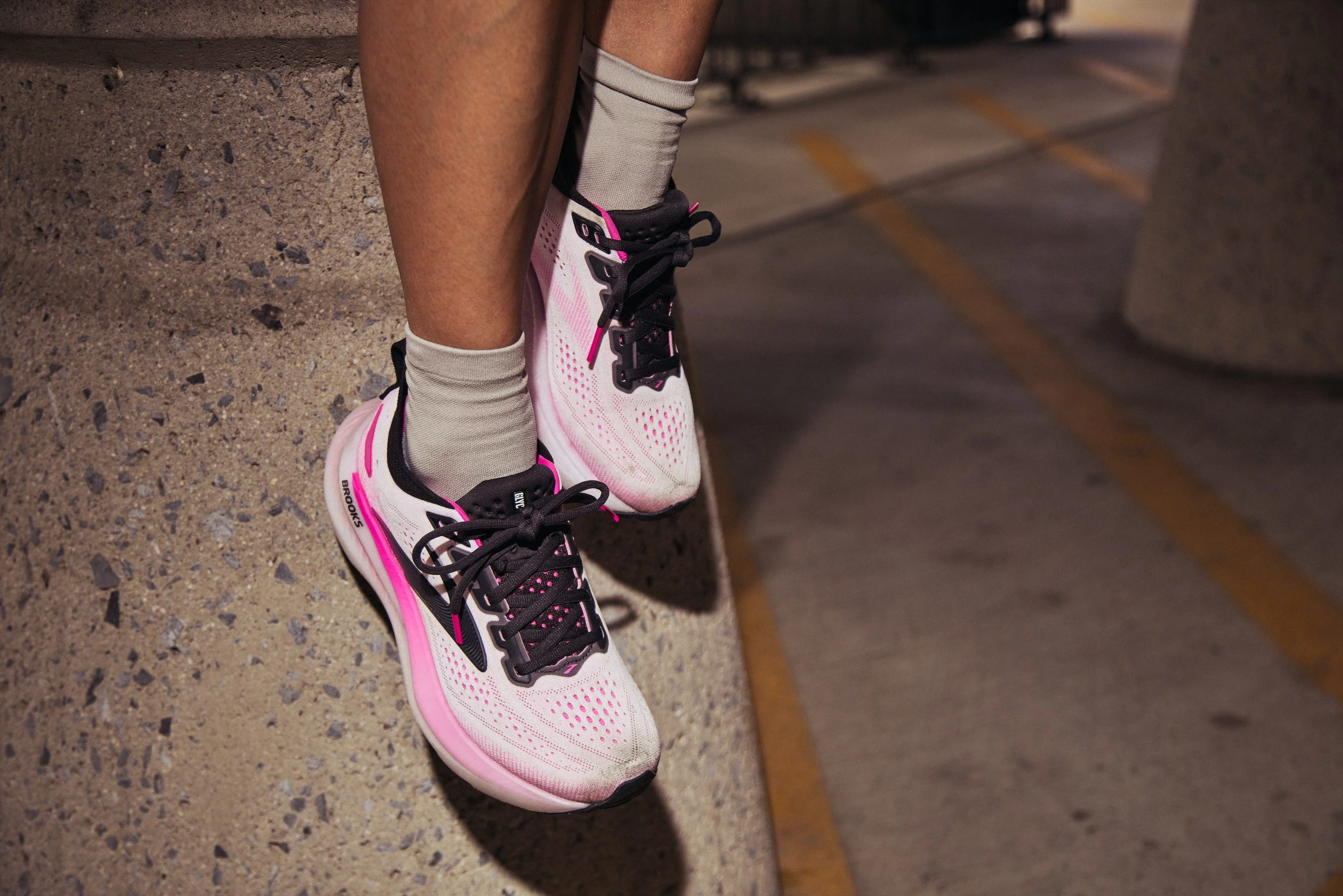 Pink and white running shoes on feet, resting against a concrete surface. Pink and white running shoes on feet, resting against a concrete surface.