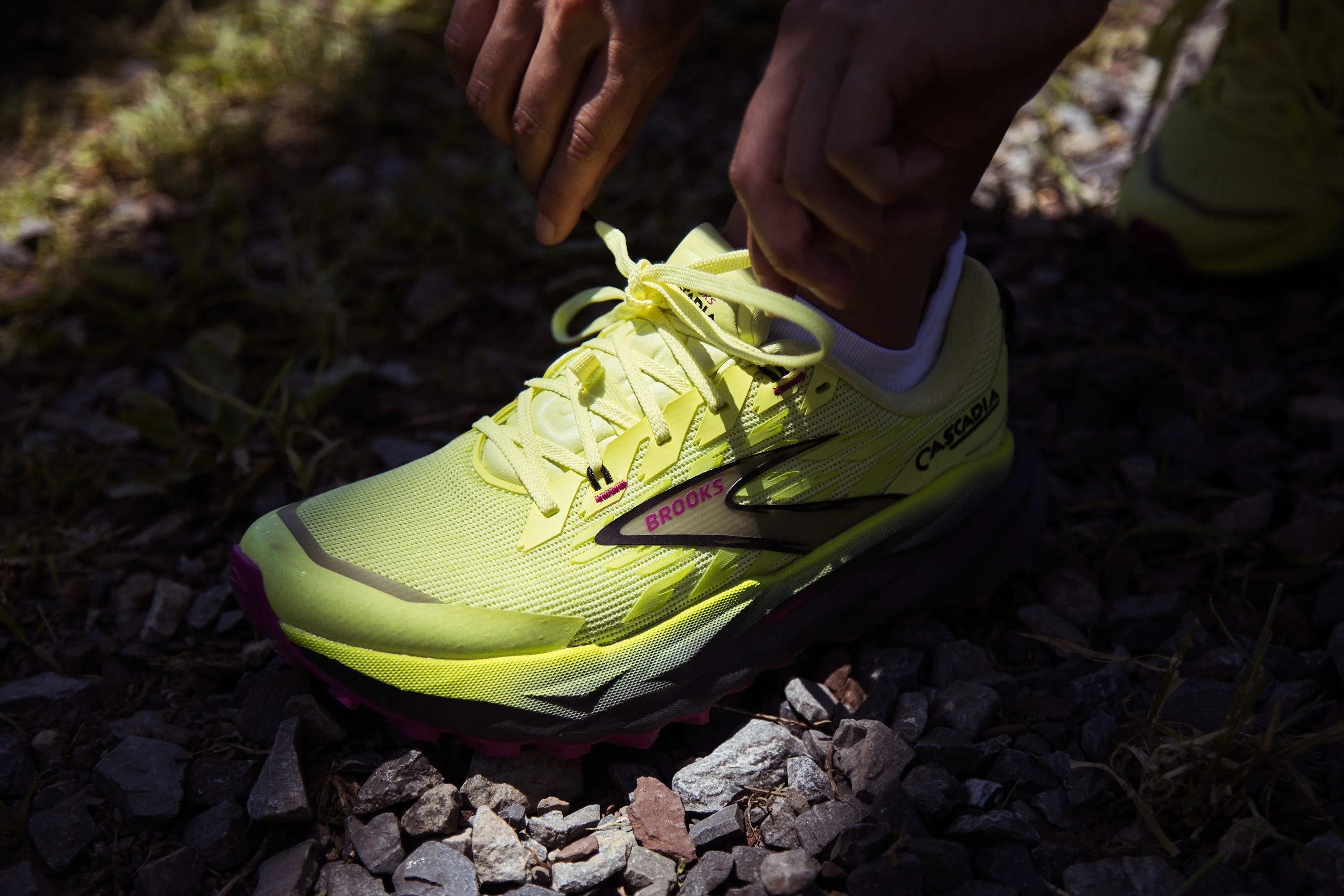 Person tying laces on a bright yellow Brooks running shoe on gravel. Person tying laces on a bright yellow Brooks running shoe on gravel.