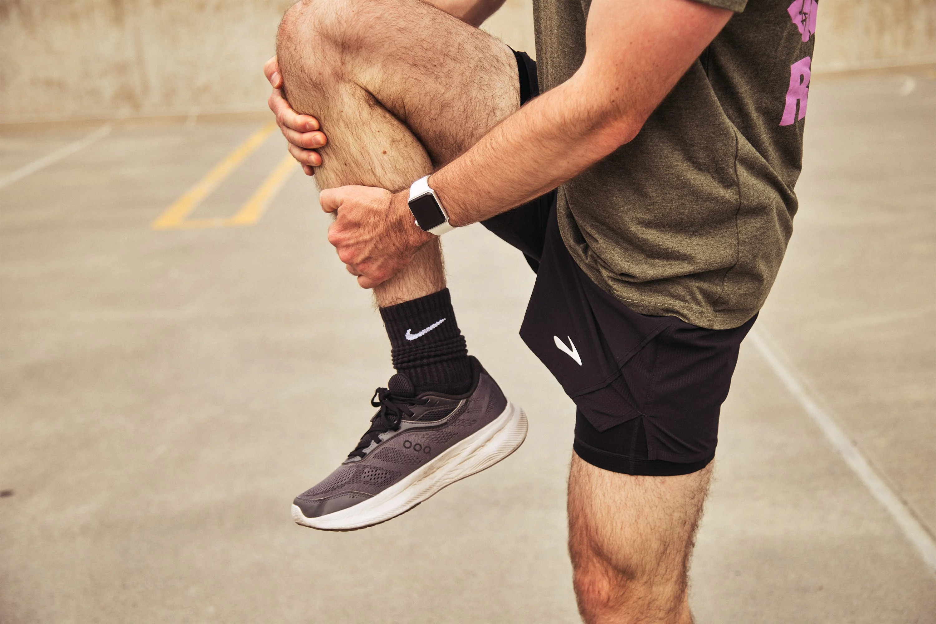 Runner stretching leg on a concrete surface wearing shorts and athletic shoes. Runner stretching leg on a concrete surface wearing shorts and athletic shoes.
