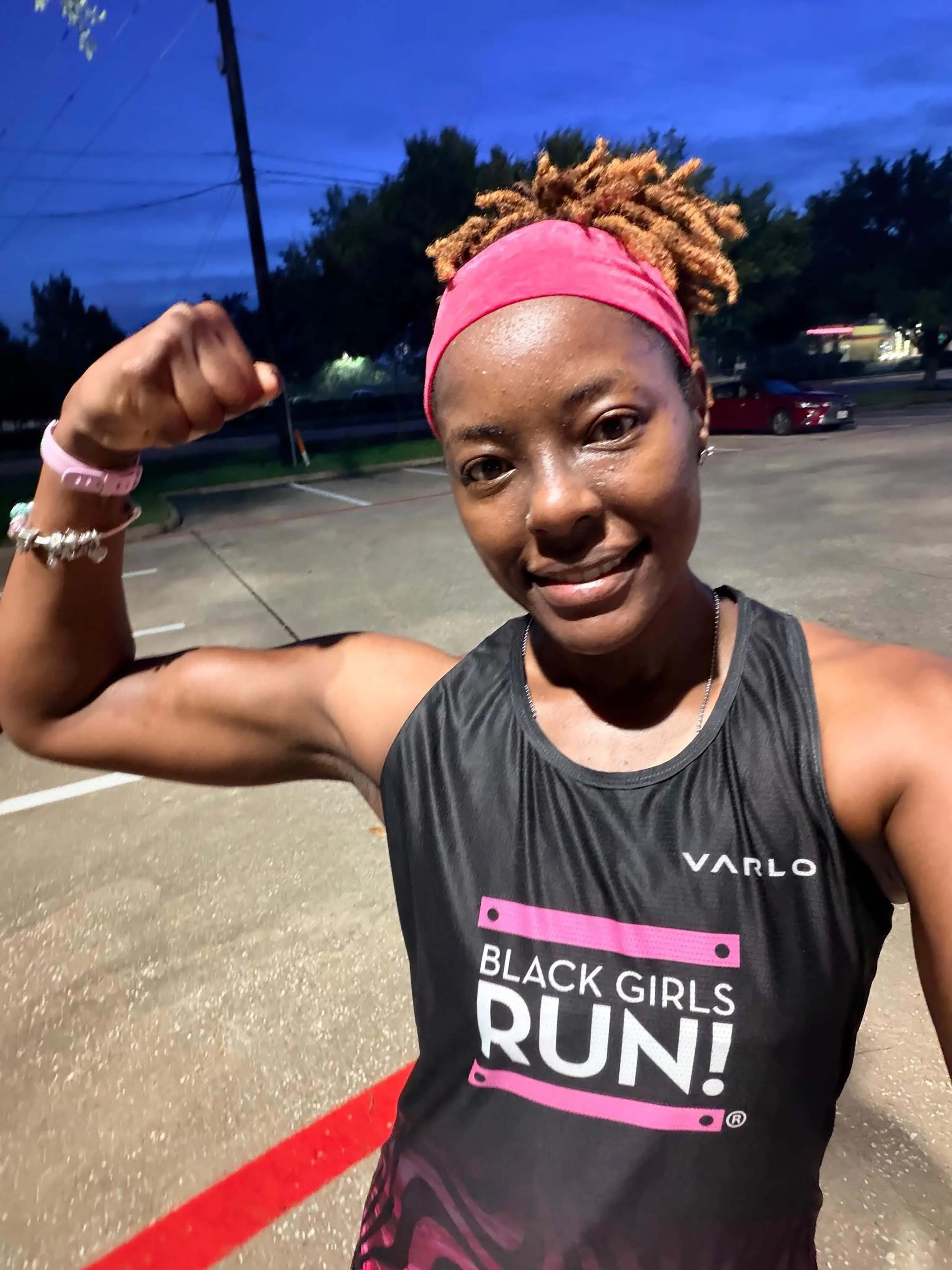 Runner smiling, wearing "Black Girls RUN!" tank top, flexing arm in outdoor setting. Runner smiling, wearing "Black Girls RUN!" tank top, flexing arm in outdoor setting.